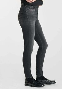 Jean skinny noir taille haute en denim, avec une poche avant ornée et un détail texturé à l'arrière.