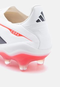 Λευκό ποδοσφαιρικό παπούτσι Adidas Copa με κόκκινη σόλα και τάπες, μαύρο λογότυπο Adidas στη φτέρνα και κόκκινο κείμενο "COPA" στο πλάι.