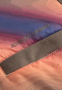 Farebná tkanina s prechodom od ružovej po modrú, s textúrovaným hnedým popruhom a vyrazeným textom "JOHNNY URBAN" jasne zobrazeným.