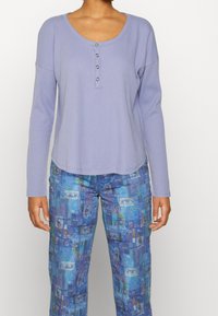 Ljuslila långärmad skjorta med en rundad halsringning och tre knappar. Matchas med blå byxor med en kollage av ögon och abstrakta mönster.