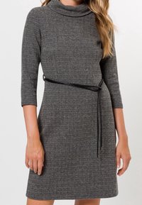 Robe en chevrons gris avec un col drapé, des manches trois-quarts et une ceinture noire soulignant la taille. Texture lisse, coupe ajustée.