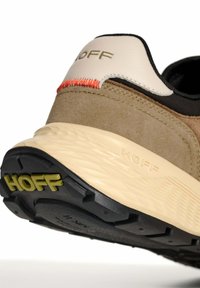 Acercamiento de un talón de zapatilla HOFF en tonos beige y marrón, mostrando la suela texturada, la parte superior cosida y el logo de la marca en la suela y en la etiqueta del talón.