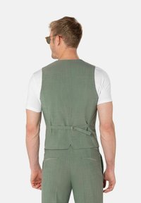 Hellgrüner, strukturierter Weste mit angepasstem Rücken, verstellbarem Schnallendetail, getragen über einem weißen Hemd, das ein minimalistisches Design präsentiert.