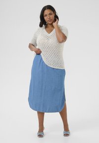 Leichter, cremefarbener Strickpullover mit V-Ausschnitt und kurzen Ärmeln, kombiniert mit einem knielangen Jeansrock mit seitlichen Schlitzen.
