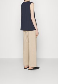 Námořnický bezrukávový top z měkké bavlny s volnými béžovými lněnými kalhotami. Černé ploché slip-on boty dotvářejí touto outfit.