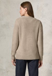 Beige neulepaita, jossa on ribattu pinta, pyöreä kaula-aukko ja pitkät hihat, ulottuen lantiolle. Yhdistetty tummansinisiin farkkuihin.