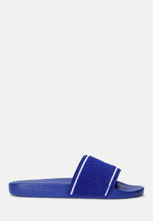 Blaue Slide-Sandale mit strukturiertem Fußbett und breitem Frottee-Riemen mit zwei weißen vertikalen Streifen, in Seitenansicht vor weißem Hintergrund.