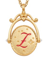 Gouden medaillonketting met de letter "L" in het rood, steraccenten en een gestructureerd ovaal ontwerp. Afgewerkt met decoratieve beslag en kleine pareltjes.