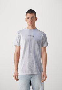 Fehér pamut póló rövid ujjal és kerek nyakkivágással. A mellkas közelében fekete színnel "SANTA CRUZ" felirat látható. Egyszerű design, laza szabás.