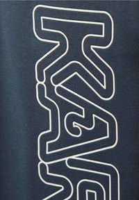 Zbliżenie na ciemny materiał z białymi konturami stylizowanego tekstu tworzącymi abstrakcyjne kształty geometryczne.