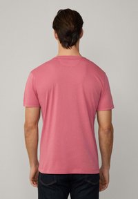 Roza majica s kratkim rukavima izrađena od mekanog pamuka, s klasičnim okruglim izrezom i ravnim rubom. Vidljivi šavovi duž rukava i struka.