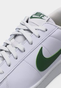 Λευκό αθλητικό παπούτσι Nike με πράσινο λογότυπο Swoosh και αντίστοιχο πράσινο κείμενο Nike στη γλώσσα, με λευκά κορδόνια και ραφές λεπτομέρειες.