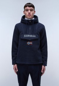 Pullover in felpa navy con cappuccio, zip frontale e toppa con logo. Presenta un piccolo dettaglio della bandiera norvegese e polsini a costine. Texture morbida.