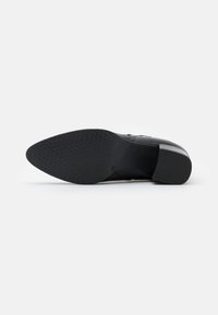 Suela de zapato negro de tacón alto con una superficie lisa y una banda de rodadura de goma texturizada. Presenta una puntera redondeada y un tacón cuadrado. Talla marcada como 39.