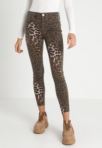Jeans skinnies de estampado de leopardo con una base marrón y manchas negras, diseño de cintura alta y un ajuste ceñido, combinados con zapatillas beige.