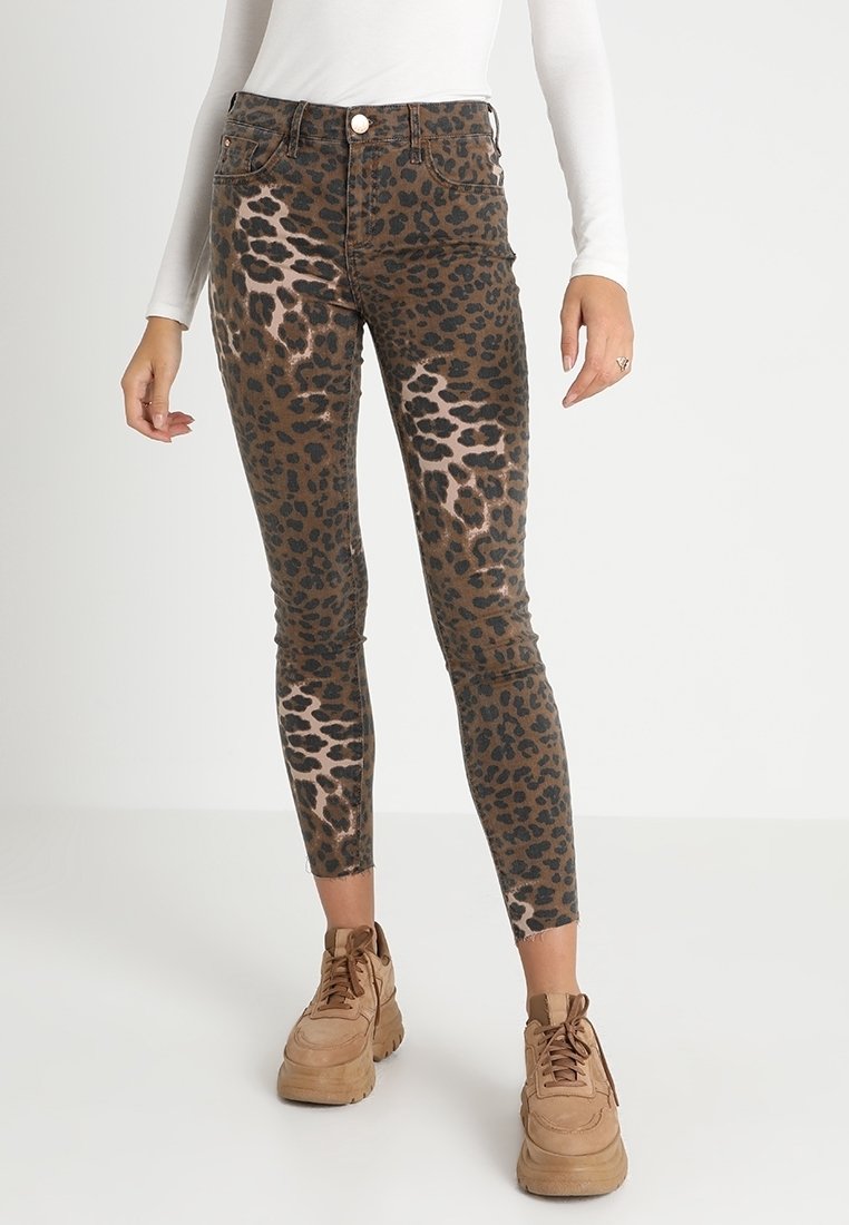 Jeans skinnies de estampado de leopardo con una base marrón y manchas negras, diseño de cintura alta y un ajuste ceñido, combinados con zapatillas beige.