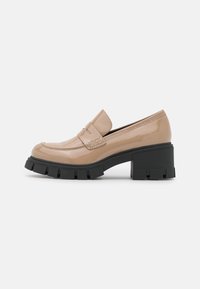 Mocassins en cuir verni beige avec une sangle texturée, un talon noir épais et un bout rond. Équipés d'une semelle à profil prononcé pour une meilleure adhérence.