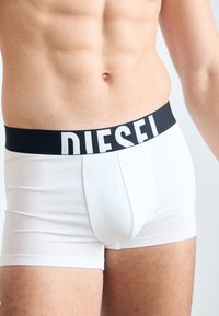 Weiße Boxershorts mit einem schwarzen Bund, auf dem "DIESEL" in fetten weißen Buchstaben steht. Der Stoff wirkt glatt und enganliegend.