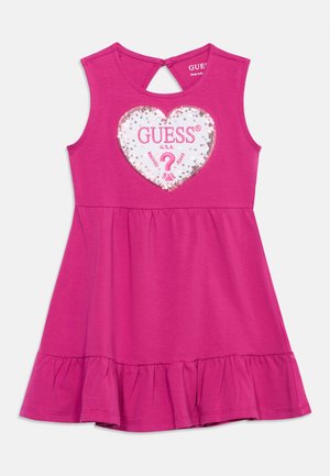 Rankovių neturinti ryškiai rožinė mažylio suknelė su raukšlėtu kraštu ir baltu blizgančiu širdies atspaudu su užrašu „GUESS U.S.A.“ priekyje.