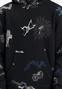 Svart hoodie med olika grafiska tryck, inklusive tärningar, lågor, ett spindelnät och ett kors, med en framficka och mjuk textur.