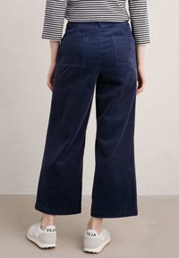 Marinblå kordflodbyxor med vida ben, fram- och bakfickor, strukturerad tyg, ihop med vita sneakers med svart logotyp på hälen.