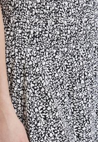 Tessuto a fiori in bianco e nero con corpetto arricciato e design plissettato, che mette in evidenza una superficie texturizzata e delicate forme di foglie.