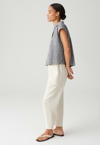 Top senza maniche grigio a righe con colletto, abbinato a pantaloni leggeri tapered color crema e sandali neri semplici.