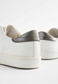 Białe sneakersy z gładką skórzaną fakturą i metalicznoszarym akcentem na pięcie. Gumowa podeszwa z subtelnymi detalami przeszycia.