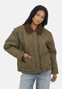 Veste matelassée vert olive avec un col en velours côtelé marron, deux poches latérales et une coupe décontractée. Présente des détails de couture ondulée.