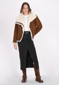 Brun ruskindsjakke med hvid pelskrave, båret over en hvid top. Sort denimnederdel med slidser foran, parret med brune knæhøje støvler.