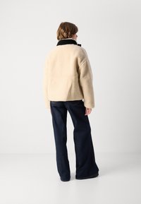 Beige fleece jas met een zwarte kraag, oversized fit en verlaagde schouders, gecombineerd met donkerblauwe flared jeans.