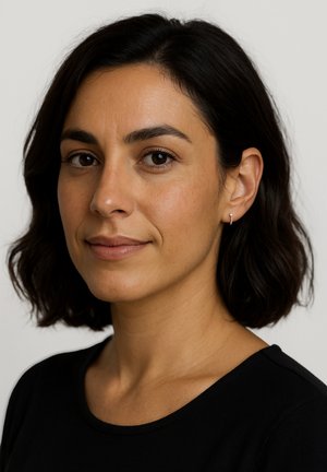Eine Frau mit schulterlangem, dunklem Haar und einem leichten Schwung, die ein schwarzes Oberteil und kleine silberne Creolen trägt, schaut leicht zur Seite.