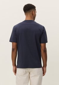 Tamsiai mėlynas medvilninis marškinėlis trumpomis rankovėmis ir apvalia iškirpte, tiesaus silueto su maža etikete kairiajame šone.