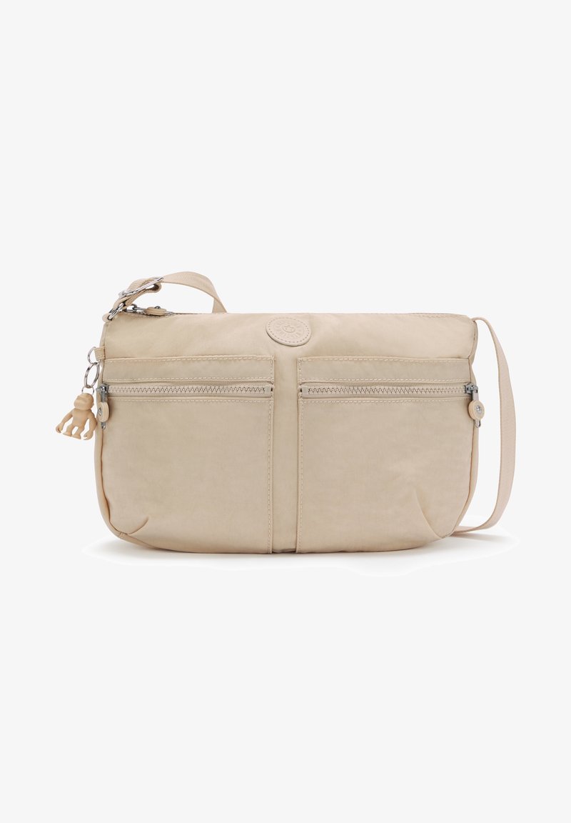 Beige fabric crossbody bag with two front zip pockets, logo patch, adjustable strap, and a decorative keychain attachment.