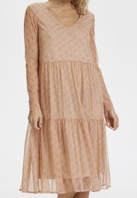 Långärmad blommig klänning med V-ringning i mjuka rosa och gula nyanser, med en flerskiktskjol och lätt, genomskinlig tygstruktur.