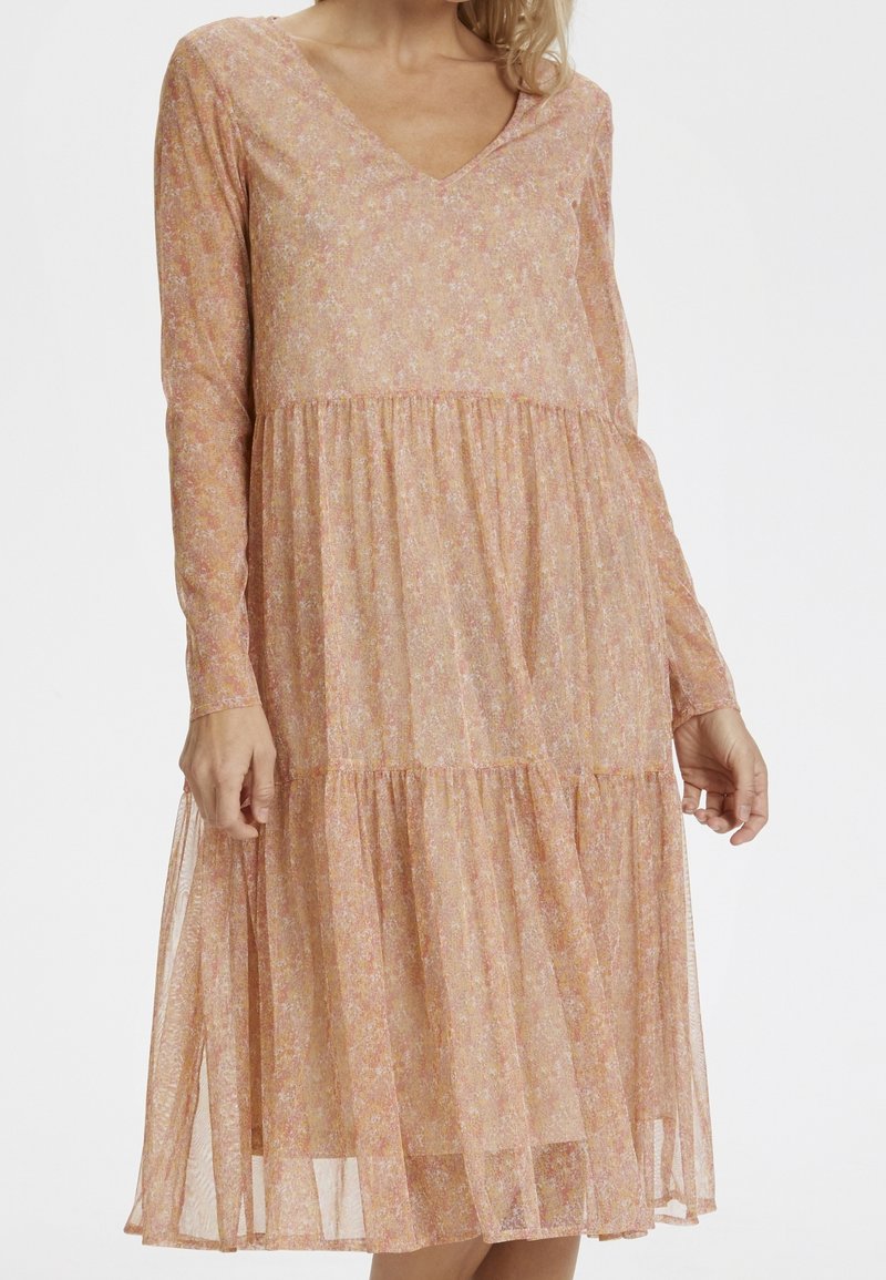 Långärmad blommig klänning med V-ringning i mjuka rosa och gula nyanser, med en flerskiktskjol och lätt, genomskinlig tygstruktur.