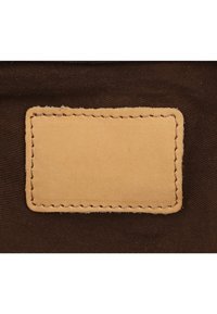 Hnedá tkanina s obdĺžnikovou béžovou koženou nášivkou, na ktorej sú kontrastné švy okolo okrajov. Hladká textúra na koži.