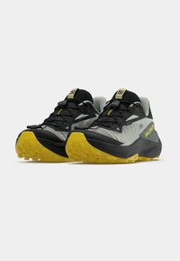 Γκρι και μαύρα παπούτσια για τρέξιμο σε μονοπάτια με κίτρινες λεπτομέ ρειες, υφασμένη σόλα και σύστημα γρήγορου δέσιμου. Ελαφρύς σχεδιασμός για υπαίθρια χρήση.