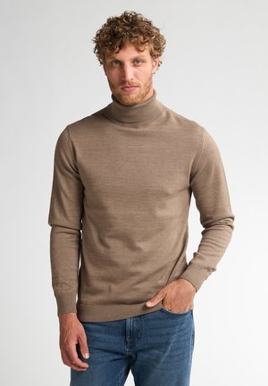 Suéter marrón de cuello alto hecho de un suave tejido de punto, con mangas largas, puños acanalados y un diseño ajustado. Se lleva con jeans azules.