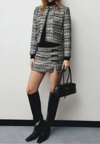 Czarna i biała tweedowa marynarka z srebrnymi guzikami, w połączeniu z dopasowaną spódnicą z panelami i rozcięciami. Czarnych, sięgających do kolan kozaków oraz torebka.