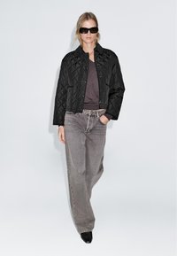 Black quilted short jacket, gray t-shirt, and high-waisted gray jeans. Model wearing black sunglasses and black pointed-toe boots.