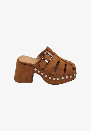 Mule en suede marron à plateforme, avec un bout ouvert, un détail de boucle et des clous décoratifs le long de la base. Design de talon épais.