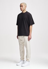 Schwarz oversized T-Shirt mit Rundhalsausschnitt und kurzen Ärmeln, kombiniert mit beigen Jogginghosen und weißen Sneakern. Glatter Stoff, lockere Passform.