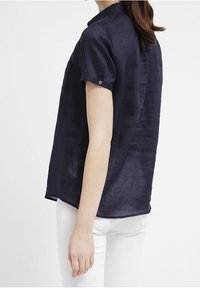 Námořnická blůza s krátkým rukávem, s detailním zapínáním na knoflíky, límečkem a volným střihem, vyrobená z lehkého materiálu, doplněná bílými kalhotami.