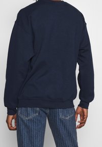 Felpa blu navy con vestibilità rilassata, polsini e orlo a coste, realizzata in morbido tessuto di cotone. Presenta una scollatura rotonda e un design minimalista.