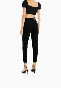 Jeans negros de tiro alto con un ajuste slim, que cuentan con bolsillos traseros y costuras sutiles, combinados con sandalias de tacón negras con tiras.