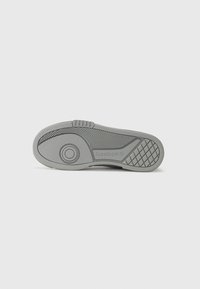 Grå gummisula med texturerade mönster, Reebok-logotyp och ett cirkulärt designelement. Har diagonala och rutnätselement för bättre grepp.
