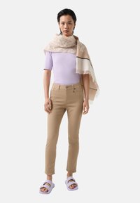 Light purple fitted top, beige fitted pants, and lavender sandals. Scarf features a subtle pattern with fringed edges, draped over shoulders.
