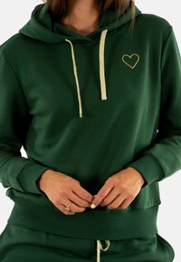 Grøn hoodie lavet af blødt stof, med guld hjerte broderi og metaltræk. Har ribbede manchetter og kant for en god pasform.