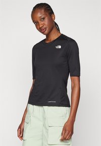 Svart kortärmad skjorta med texturerad yta och en subtil logotyp på bröstet. I kombination med ljusgröna cargobyxor med flera fickor.